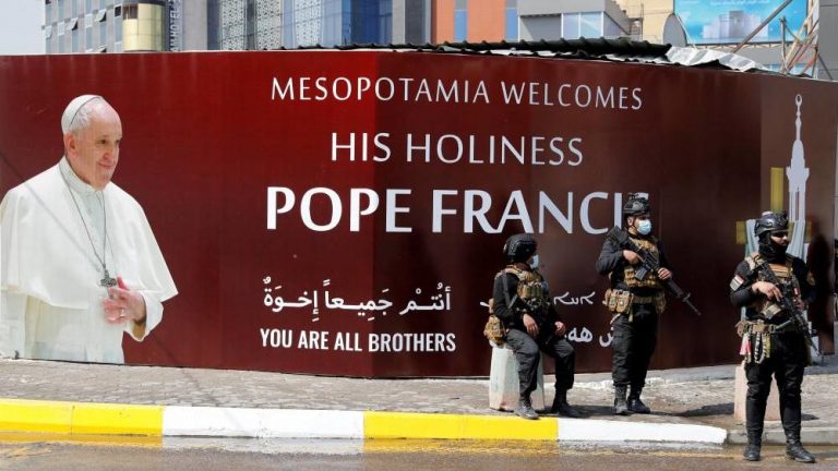 Security men are seen in front of a poster of Pope Francis ahead of the planned visit of Pope Francis to Iraq, in Baghdad